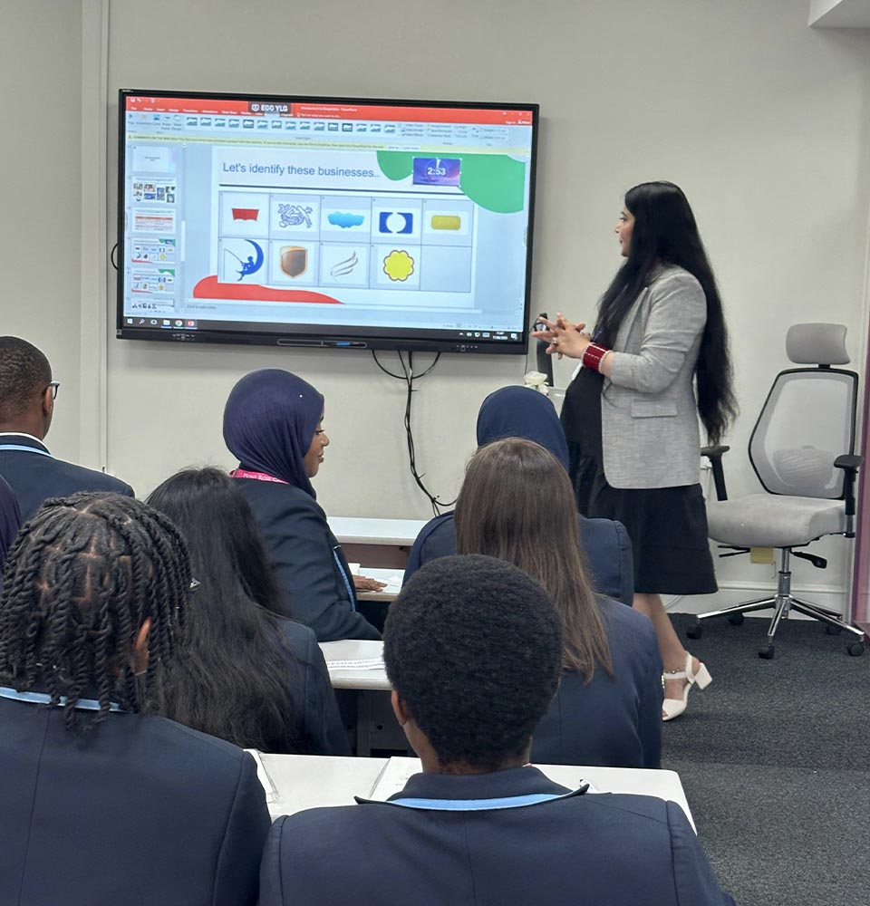 Teacher leading a classroom activity on business logos for Cumberland High School students during an educational visit.
