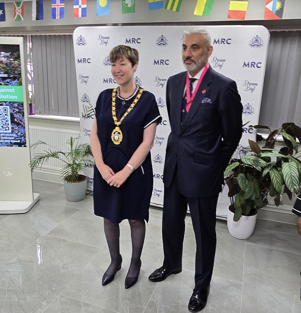 Two dignitaries posing at Mont Rose College during the Environment Day Programme, with flags and banners in the background.