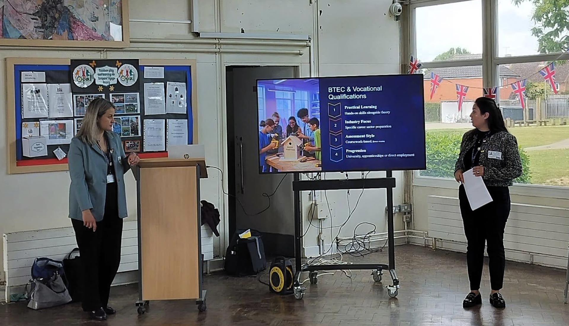 Two women giving a presentation on BTEC and vocational qualifications, outlining Higher Education pathways for students.