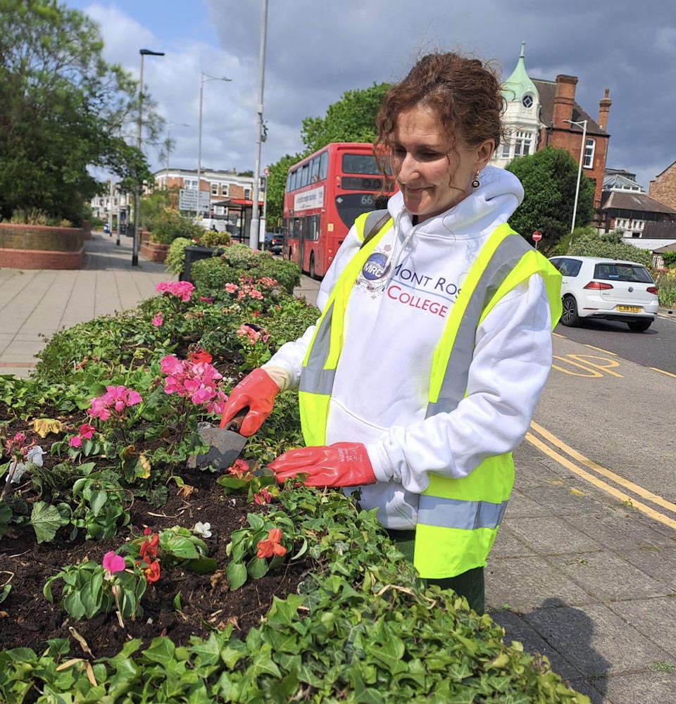 Woman in high-visibility vest planting flowers on a city street, contributing to the Greener Redbridge initiative.