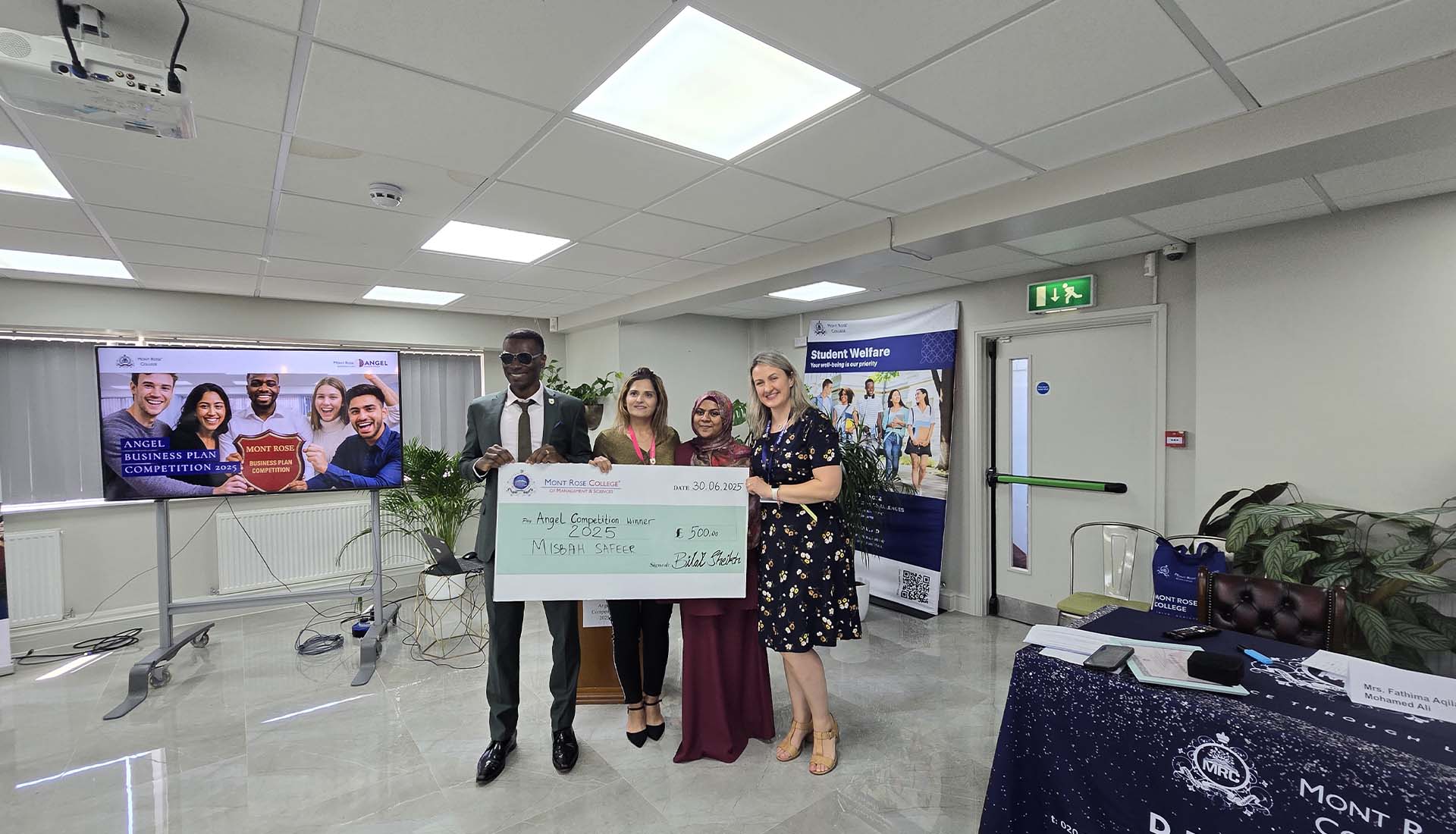 Angel Competition winner Misbah Safeer holding prize cheque with Mont Rose College staff during award ceremony celebration.