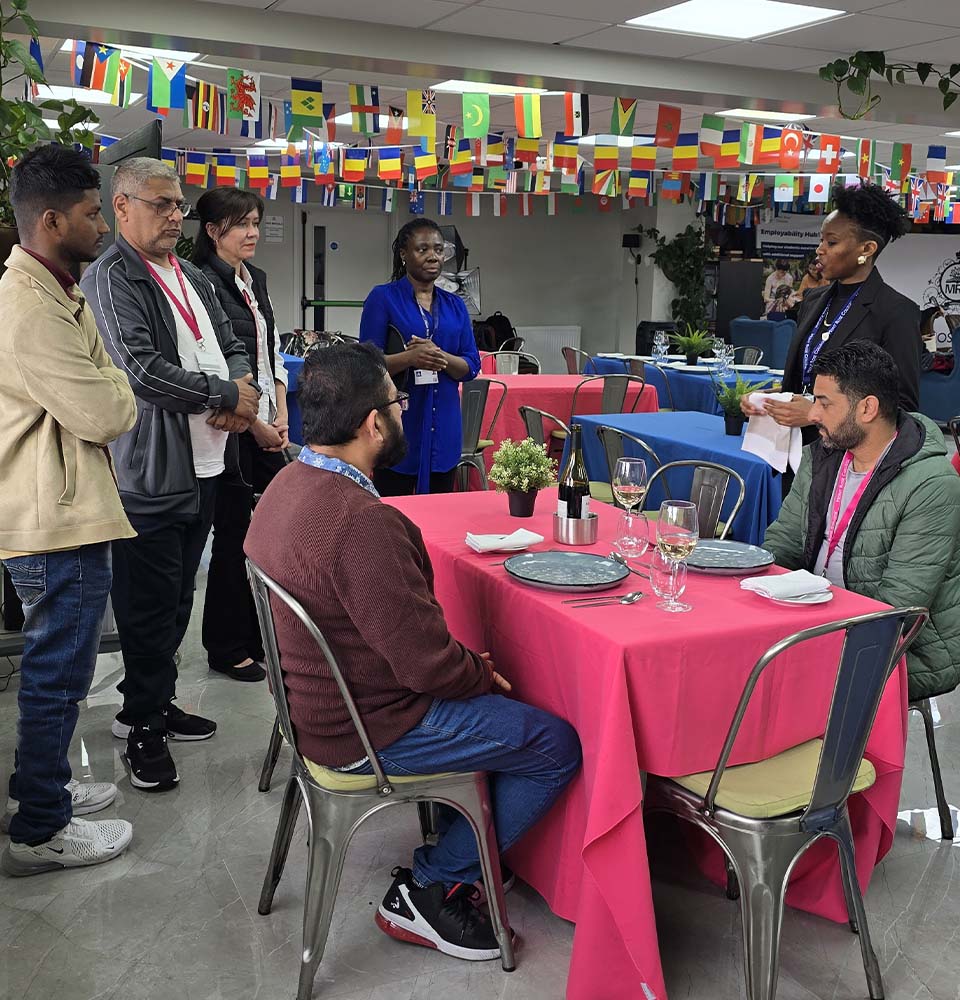 Hospitality instructor demonstrating wine service to seated participants during the Hospitality Skills Event, with others observing the training.