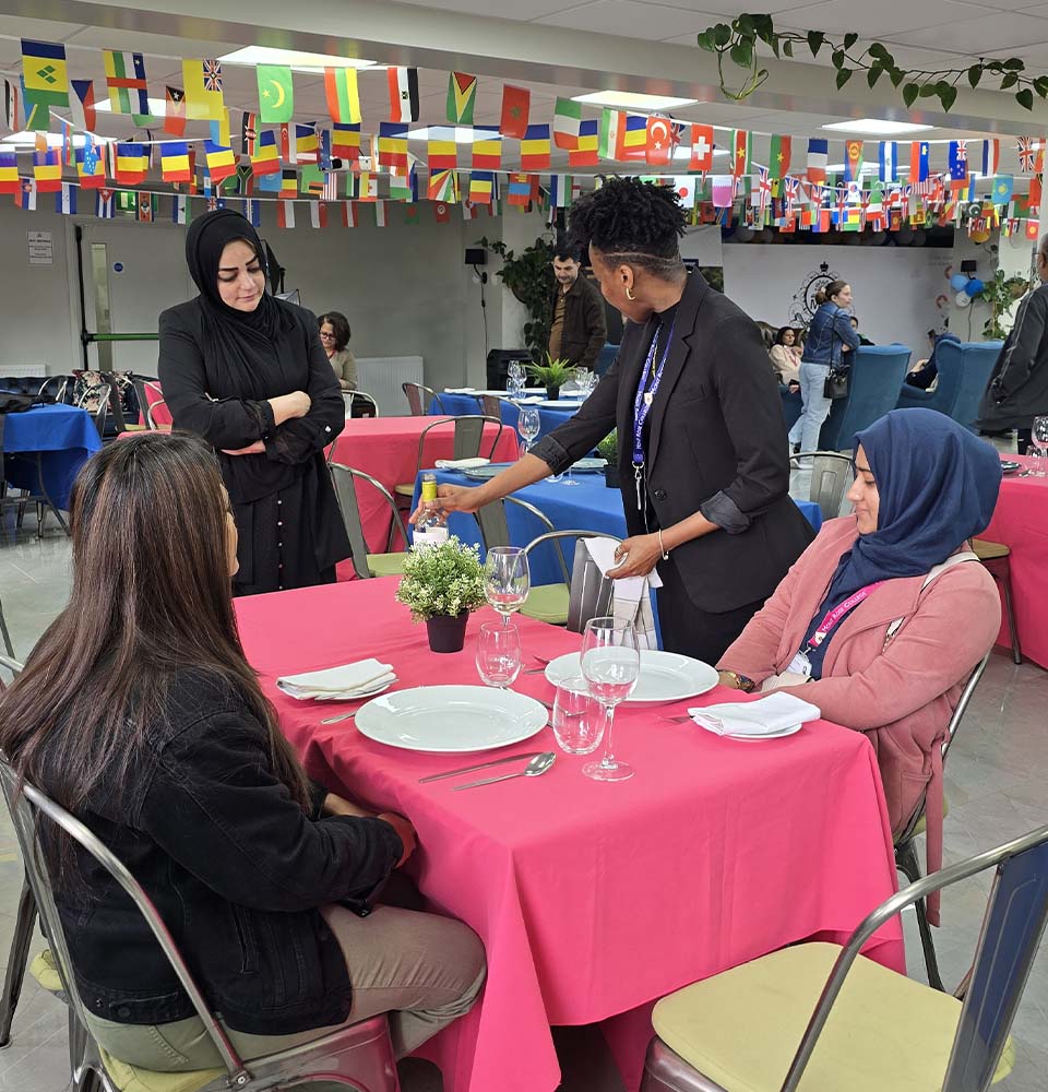 Instructor demonstrating table service to seated participants during the Hospitality Skills Event, showcasing hands-on hospitality training.