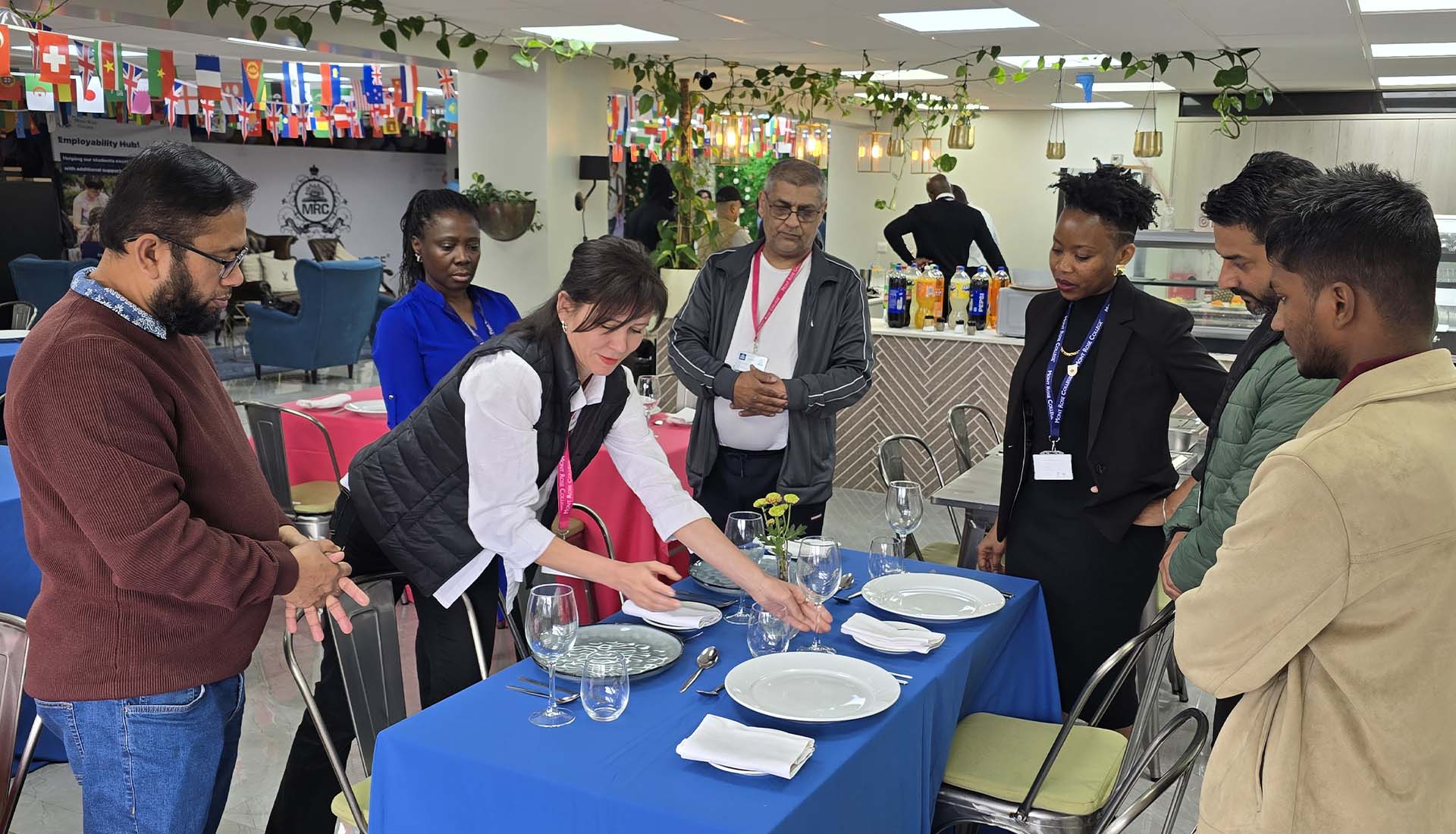 Instructor demonstrating table setting to participants during the Hospitality Skills Event, showcasing practical hospitality training in a decorated space.