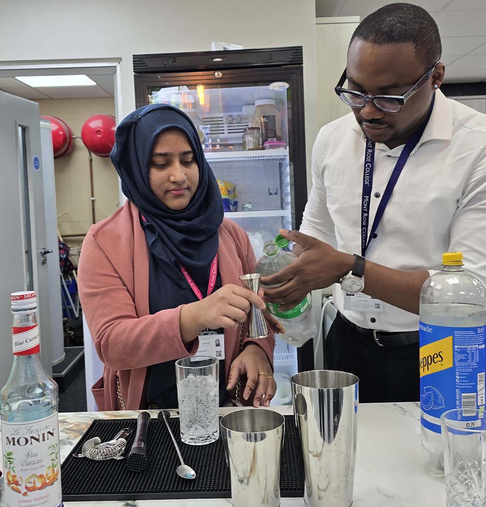 Student learning drink mixing techniques from instructor during the Hospitality Skills Event at Mont Rose College.