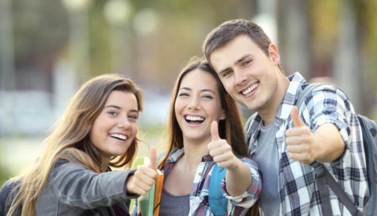 Three smiling students outdoors giving thumbs up, representing positive choices in the debate of HND vs. Continuing Education.