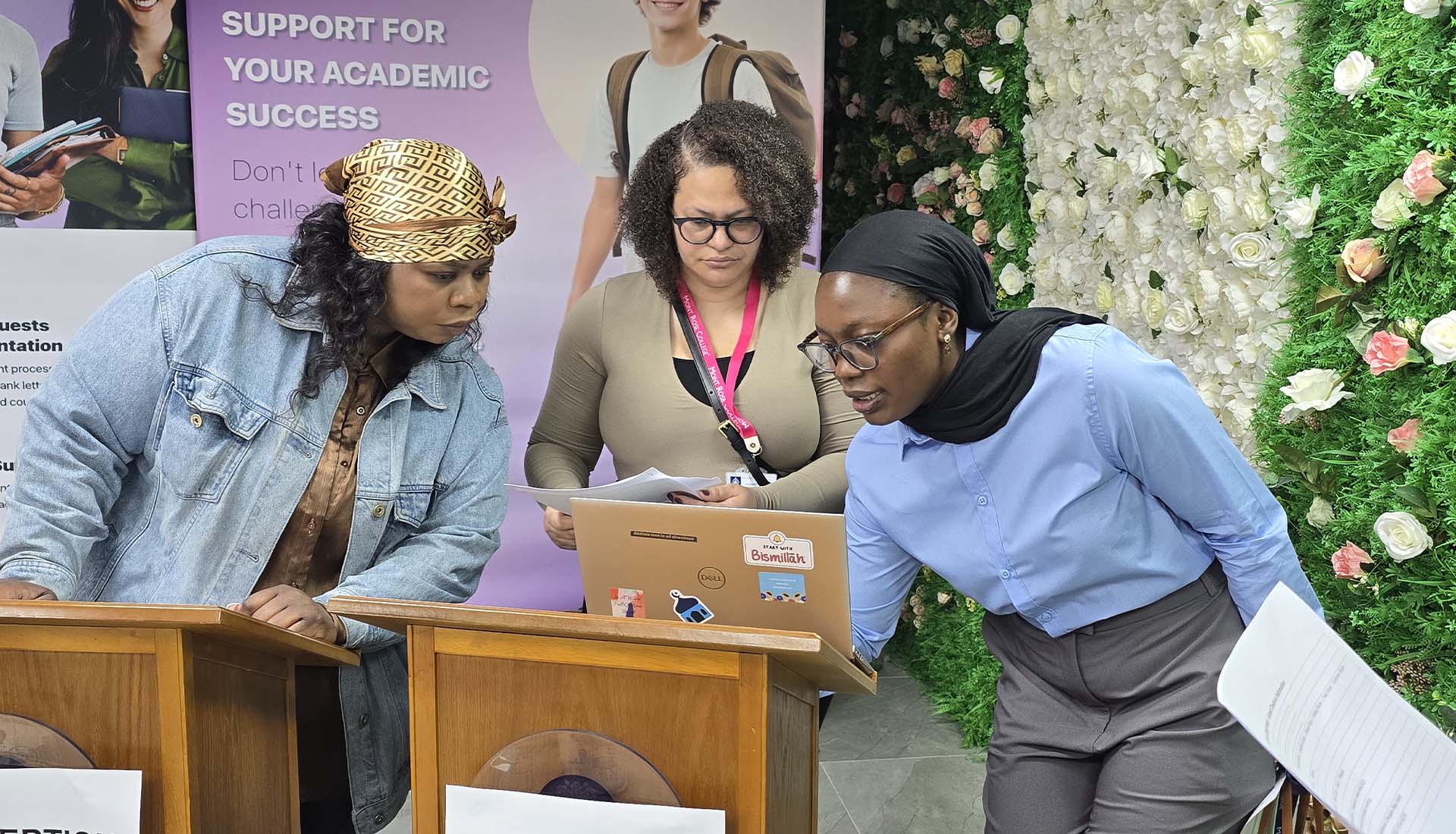 Three women reviewing documents and laptop at reception desk during the Hospitality Skills Event, promoting academic and career support.