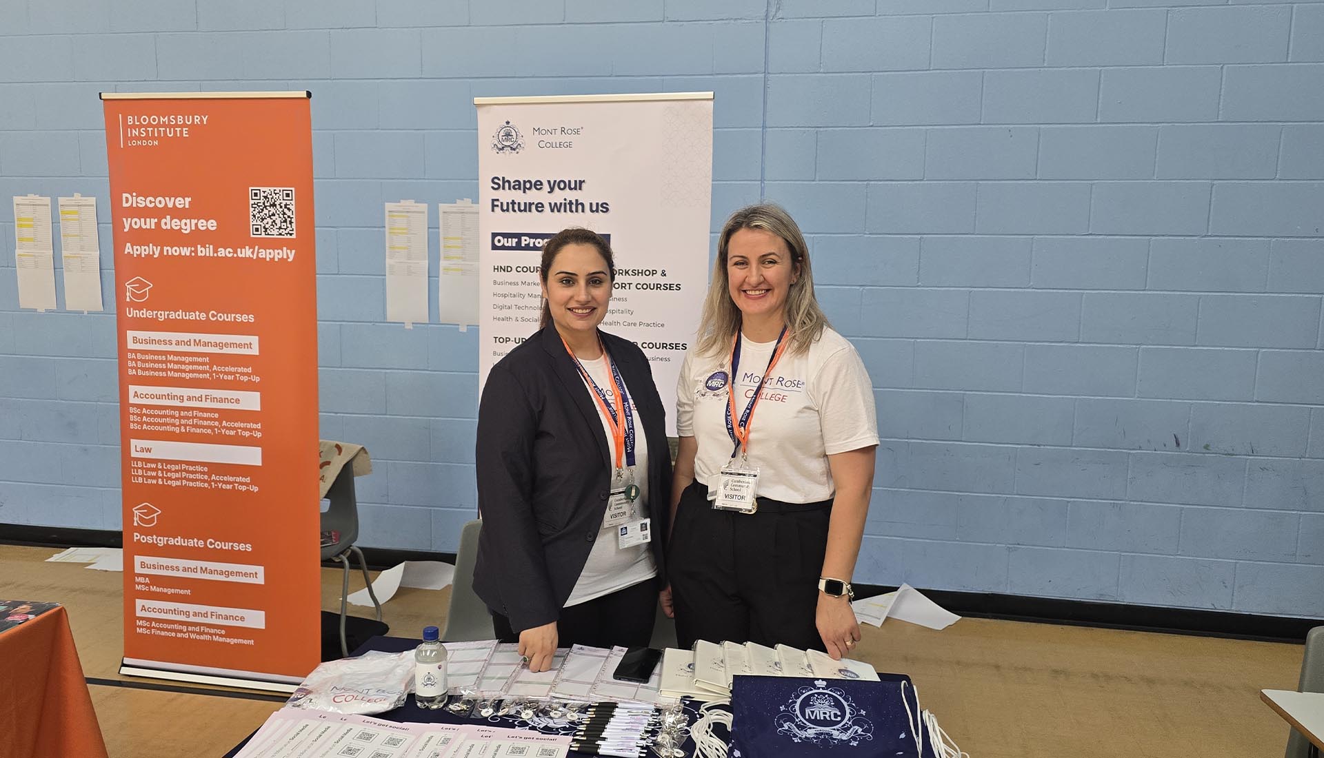 Two Mont Rose College representatives standing at a career fair booth with promotional materials, showcasing Mont Rose College career fair.
