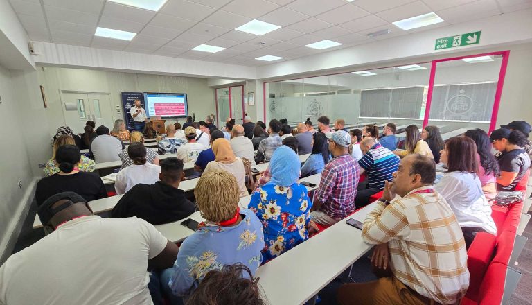 Audience attending a presentation by Matt Whittingham at Mont Rose College, with a slideshow displayed at the front.