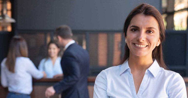 Smiling hospitality professional in uniform with colleagues in background, representing HND in Hospitality Management career opportunities.