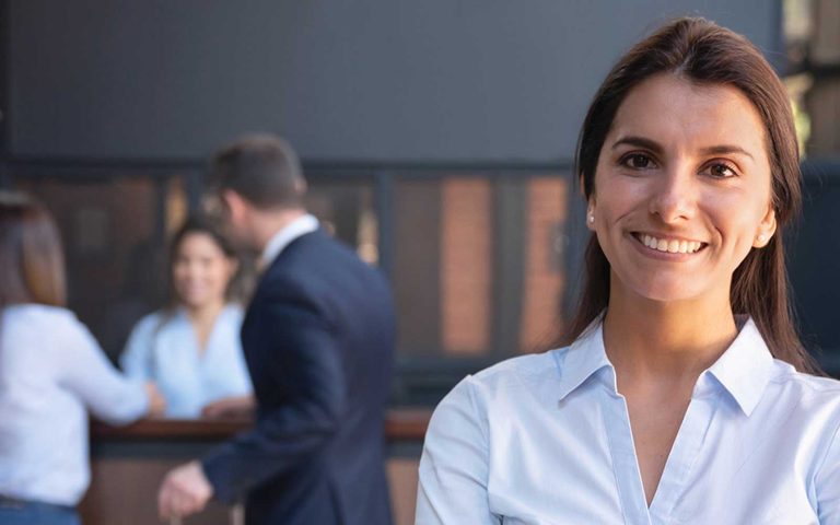 Smiling hospitality professional in uniform with colleagues in background, representing HND in Hospitality Management career opportunities.