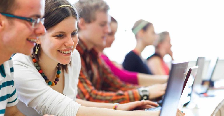 Students smiling and working on laptops in a classroom, representing HND vs. Technical Diplomas learning environments.