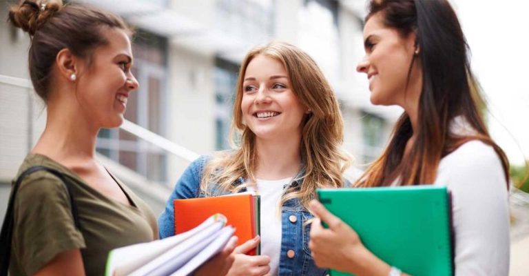 Three smiling students holding folders and chatting outdoors, representing HND in Business Management studies.