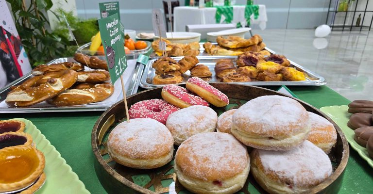 Assorted pastries and donuts displayed on a table for a Macmillan Coffee Morning fundraising event.