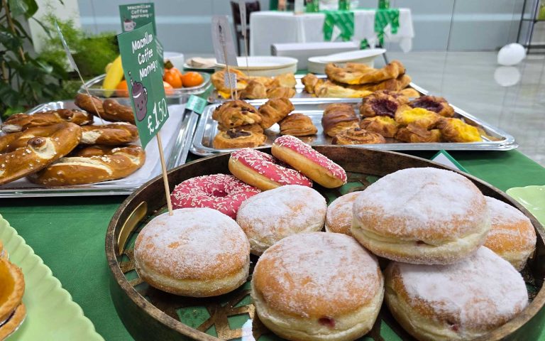 Assorted pastries and donuts displayed on a table for a Macmillan Coffee Morning fundraising event.