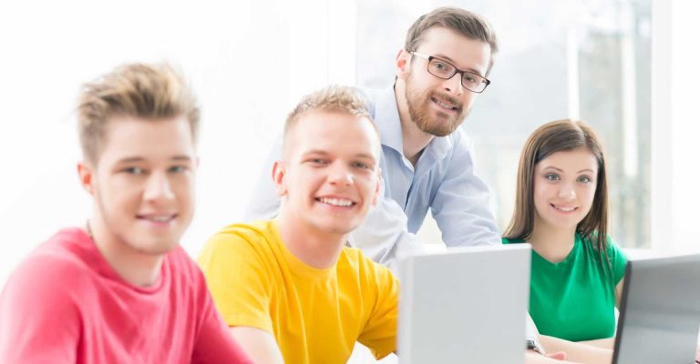 Students working on laptops with a mentor, representing writing a personal statement for HND applications.