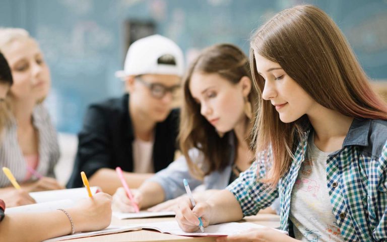 Students attentively filling out forms and writing in notebooks in a classroom setting, representing the HND application process.