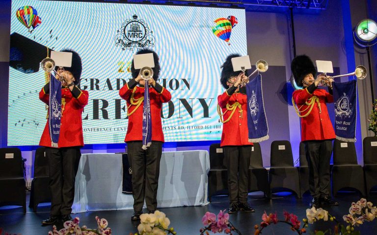 Uniformed trumpeters performing on stage during Mont Rose College Graduation 2025 ceremony, with college banners and floral decorations.
